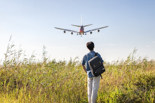 a man with a backpack looking at an airplane in the sky