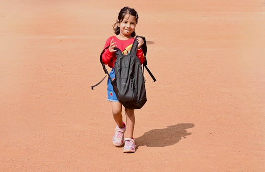 Young girl with backpack walking on sandy ground